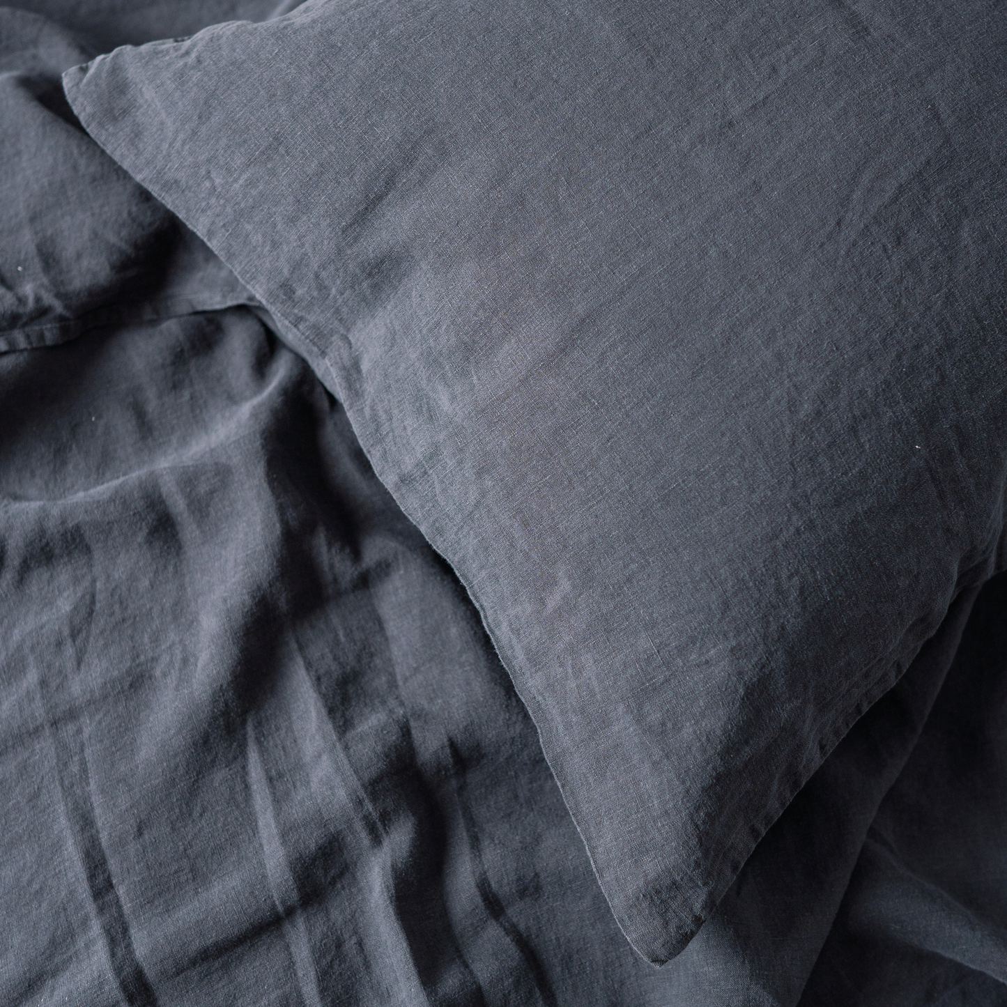 A closeup of LEWSII pillowcase on a bed in a dark grey color
