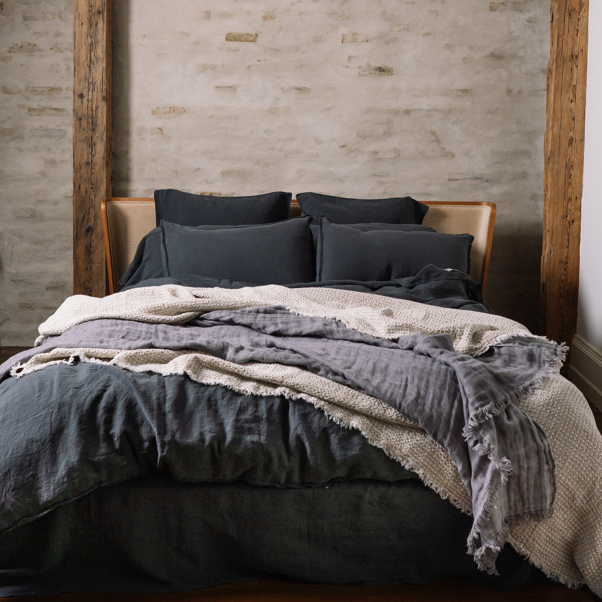 Bed covered in LEWSII bedding with a blanket. Couple of pillows in linen pillowcase in the Dark Grey color