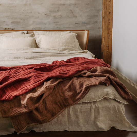 Three leyer linen blanket in rusty color seen in interior with sandy bedding set