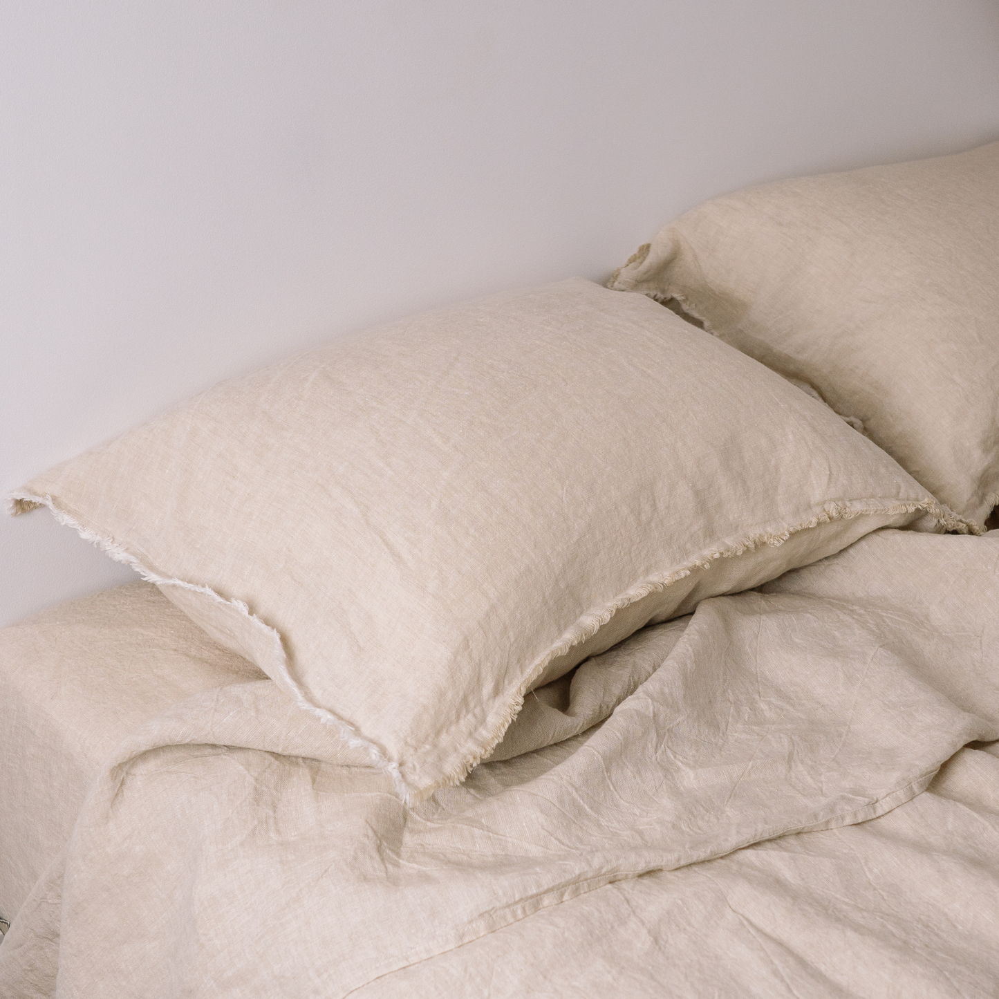 Two LEWSII pillowcases laying on a bed in the color Sandy